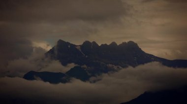 Karamsar bulutlarla kaplanmış, alacakaranlıkta güzelce yakalanmış karanlık dağ tepelerinin nefes kesici manzarası.