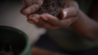 Zengin, karanlık toprağı nazikçe kavrayan, büyümeyi, beslenmeyi ve sürdürülebilirliği sembolize eden ellerin detaylı bir yakın çekimi