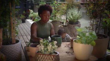 Bir kadın, çocuk yemyeşil bir ortamda mutlu mesut oynarken bahçe işleriyle uğraşmaktan zevk alır.