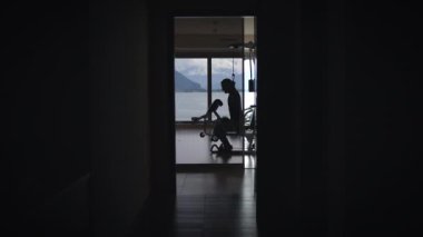 Siluetli bir figür, dağlara bakan çarpıcı bir manzara sunan geniş ve geniş bir odada çalışıyor.