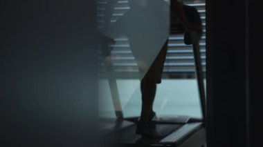 Gizemli, gölgeli bir figür, şık bir cam bariyer tarafından çerçevelenmiş bir koşu bandında enerjik bir şekilde egzersiz yaparken görülüyor.