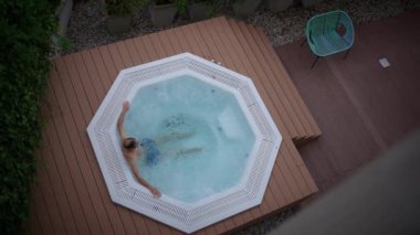 Huzurlu ve sakin bir akşam sahnesi, yemyeşil sularla çevrili sıcak bir jakuzinin keyfini çıkaran bir insanı canlandırıyor.