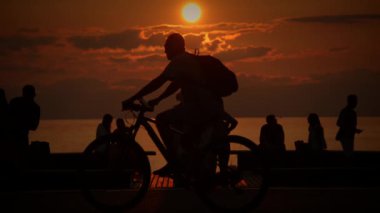 Siluetli figürler, deniz kenarında sakin bir gün batımının keyfini çıkarırlar, bir huzur ve bağlantı anını yakalarlar..