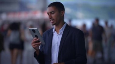 Zarif bir takım elbise giymiş genç bir adam yüksek teknoloji cihazıyla meşgul olurken enerjik bir kalabalık etrafını sardı.