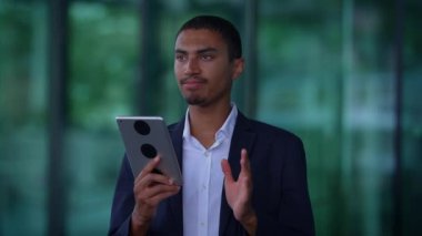 Keskin takım elbiseli odaklanmış genç bir adam, modern bir iş ortamında dijital yeteneklerini gösteren parlak bir tablet kullanır.
