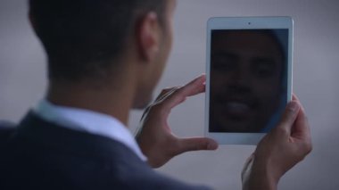 Bir adam elinde tablet tutarken kendi görüntüsünü modern ortamda yansıtan bir selfie çekiyor.