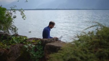 Huzurlu göl kıyısında, etrafı tamamen doğa ve görkemli dağlarla çevrili bir adam işine barışçıl bir şekilde bağlıdır.