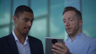 Çağdaş bir ofis ortamında, iki profesyonel tablet kullanan bir proje hakkında ayrıntılı bir tartışmaya giriştiler.