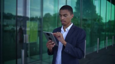 Kendini işine adamış ve odaklanmış genç bir profesyonel modern bir şehir binasının dışında şık bir tabletle aktif olarak meşgul oluyor.