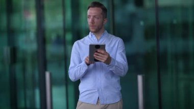 Bir adam, kentteki gösterişli ve modern cam bir binanın önünde otururken tabletine derinden bağlıdır.