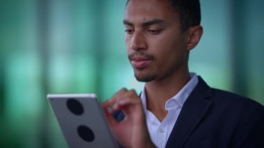Odaklanmış bir işadamı, çağdaş ve modern bir ofis alanında çalışırken bir tabletle derinden ilgilenir.
