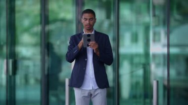 Modern, parlak, cam kaplı bir ortamda tabletle aktif olarak ilgilenen başarılı bir profesyonel adam.