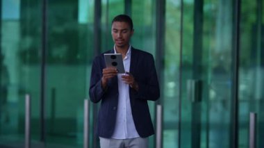 Genç bir adam modern ofis ortamında akıllı telefonunu kullanırken mutlu bir şekilde gülümsüyor.