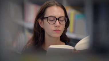 Kendini adamış bir okuyucu, çok hareketli bir kütüphane ortamında büyüleyici bir kitaba kendini kaptırmış durumda.