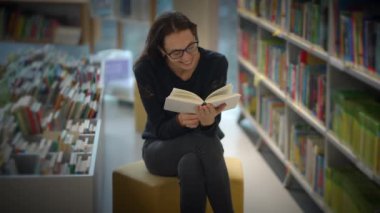 Bir kadın, modern bir kütüphanede derin düşüncelerine dalmış bir şekilde otururken büyüleyici bir kitapta kaybolur.
