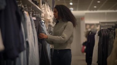 Bir kadın modern bir perakende mağazasında alışveriş yaparken farklı kot seçeneklerini dikkatle araştırır.