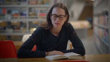 Genç bir kadın, huzurlu bir kütüphane ortamında büyüleyici bir kitap okumakla meşgul.