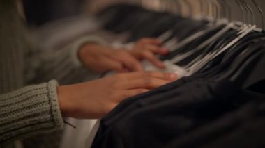 Hareketli bir elbise askısı üzerinde çeşitli kumaşları nazikçe keşfeden ve hisseden ellerin yakın görüntüsü