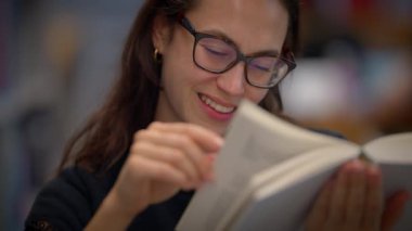 Bir kadın büyüleyici bir kitap okurken ışıl ışıl gülümser, kendini harika bir neşe ve keşfe kaptırır.