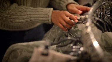 Eller şık bir butikte askılarda sergilenen şık kıyafetleri keşfeder, moda alışverişinin özünü gözler önüne serer.
