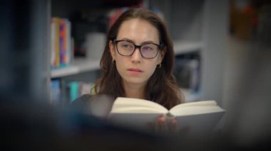 Odaklanmış genç bir kadın, etrafı davet edilen bir kütüphane zeminiyle çevriliyken tamamen bir kitap okumakla meşgul.