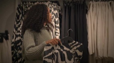 Genç bir kadın şık bir moda mağazasında şık giyim seçeneklerini gözden geçiriyor.