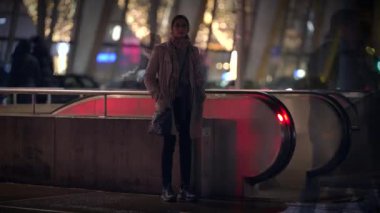 Geceleri canlı bir şehirde, parlak ışıklarla aydınlatılan ve kentsel elementlerle çevrili yalnız bir şahsiyet.