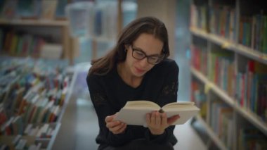Genç bir kadın enerji dolu canlı ve renkli bir kütüphane atmosferinde kitap okumaktan mutlu.