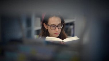 Genç bir kadın sakin ve sakin bir kütüphane ortamında büyüleyici bir kitap okumaya dalmış.