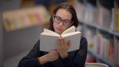 Bir kadın, sakin bir kütüphanede, okuma ve öğrenme zevkini gösteren büyüleyici bir kitaba dalmış.