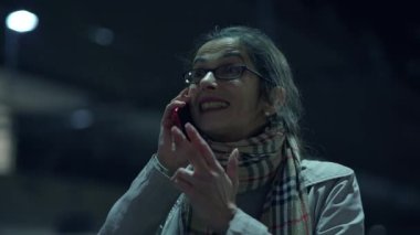 A joyful woman makes a phone call at night, surrounded by vibrant city lights in a lively urban setting