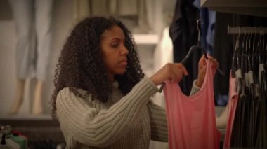 Bir kadın moda mağazasında kıyafetleri karıştırıyor, çeşitli moda tarzlarını ve seçenekleri vurguluyor