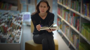 Bir kadın, hoş ve davetkar bir kütüphane atmosferinde ilginç bir kitap okurken derin bir düşünceye dalmıştır.