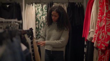 Genç bir kadın canlı stillerle dolu bir butikte moda kıyafet seçeneklerini keşfediyor.