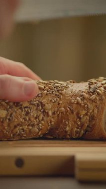 Kabuklu bir zanaatkar ekmeğine uzanan bir elin yakın çekimi tohumlu ve dokulu yüzeyini sergiliyor.