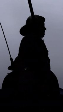 İki siluetli figür, düz gri bir arkaplana karşı gergin bir etkileşim içinde, gerilim yaratıyor.