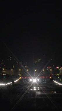 Büyüleyici bir gece sahnesi. Karanlık bir şehrin arka planında parlayan farlarıyla çok sayıda araba sergiliyor.