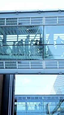 Bir ofis binasının içinden geçen büyük, çağdaş bir cam geçit, insanların hareket halindeki hareketlerini gösteriyor.
