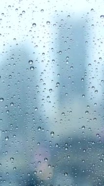 Güzel, bulanık bir manzara penceredeki yağmur damlalarının arasından yüksek binaları gösteriyor, kasvetli bir şehir atmosferi yaratıyor.