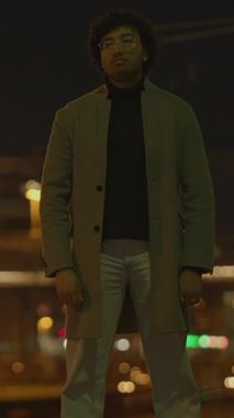 Şık bir birey, hareketli bir gece arkaplanına karşı özgüvenle duruyor, büyüleyici ve dengeli.