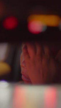 Bir insan, bir taksi içinde yüzünü gizler ve aydınlatıcı şehir ışıkları altında derin duygular gösterir.