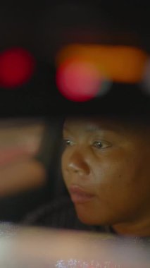 Şehir ışıklarından yansıyan parlak yansımalarla dolambaçlı bir gece yoluna odaklanmış kendini işine adamış bir sürücünün yakın çekimi.