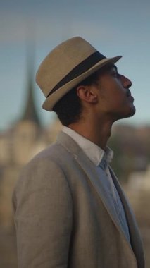 Şık ve şık bir adam dikkatle yukarı bakıyor, zarafetini ve tarzını canlı bir şehir ortamında sergiliyor.