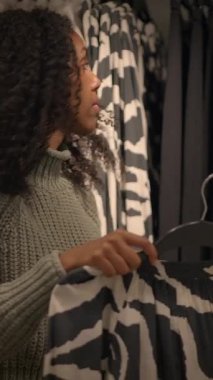 Parlak renkli bir perakende mağazasında bir kadın dikkatlice çeşitli giyim ürünlerini inceliyor.