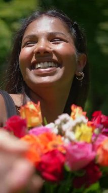 Parlak bir gülümsemesi olan neşeli bir kadın güzel bir açık hava ortamında büyüleyici bir buket taze çiçek sergiliyor.