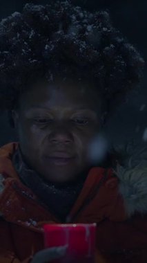 Bir insan, serin kış havasında sıcaklık uyandıran, karlı bir arazide parlayan kırmızı bir muma odaklanır.