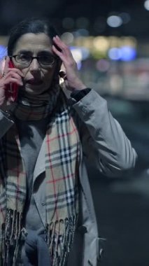 Görünürde endişeli bir kişi telefonda konuşuyor, canlı ve hareketli bir şehir manzarasına karşı.