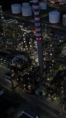 Parlak bir endüstri bölgesinin havadan görünüşü, çok sayıda depolama tankıyla birlikte uzun bir bacayı gösteriyor.