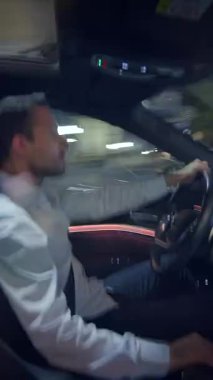 Gece boyunca araba süren bir adam, şık bir arabanın içini canlı şehir ışıklarına karşı güzelce sergiliyor.
