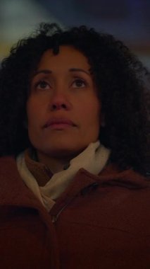 Bir kadın düşünceli bir şekilde yukarı bakar, sakin bir şehir gece sahnesinin arka planına karşı düşüncelerinde kaybolur.